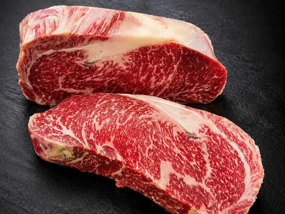 Zwei stark marmorierte Wagyu-Roastbeef-Stücke auf dunklem Schiefer